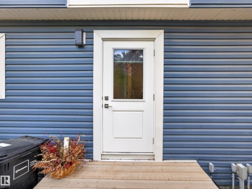 White entry door with a multi-pane window set within blue horizontal siding - 12604 116 Avenue, Edmonton, AB 