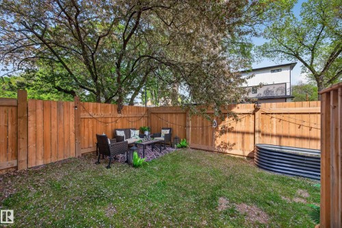 Private fenced backyard featuring a grassy area, mature trees, and a dedicated patio space with string lighting - 12604 116 Avenue, Edmonton, AB 