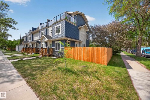 Modern townhome exterior featuring blue and white siding, stone veneer accents, and a third-story rooftop deck with glass railings - 12604 116 Avenue, Edmonton, AB 