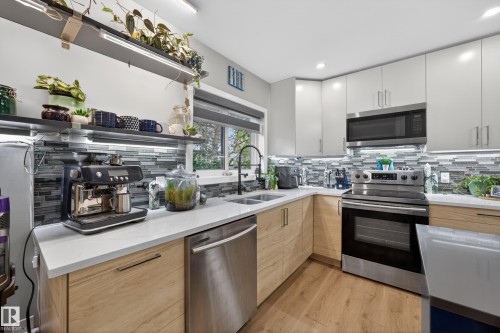 Modern kitchen featuring light wood-finish lower cabinetry, white upper cabinetry, stainless steel appliances, a mosaic tile backsplash, and a double basin undermount sink with a black gooseneck faucet - 12604 116 Avenue, Edmonton, AB 