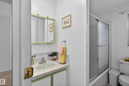 Bathroom featuring a vanity with a white countertop and integrated sink, a medicine cabinet with a light green frame, a shower-over-tub with a sliding frosted glass door, and tiled walls - 21 Willowdale Drive, Edmonton, AB - Indoor Photo Showing Bathroom