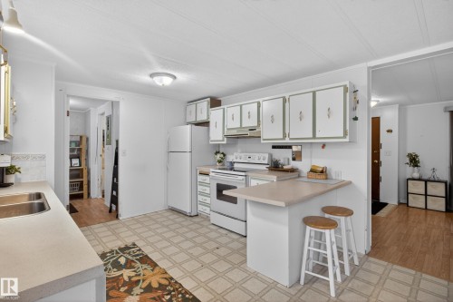 Kitchen featuring a double basin stainless steel sink, white cabinetry with decorative hardware, a built-in electric range, and a breakfast bar - 21 Willowdale Drive, Edmonton, AB - Indoor Photo Showing Kitchen With Double Sink
