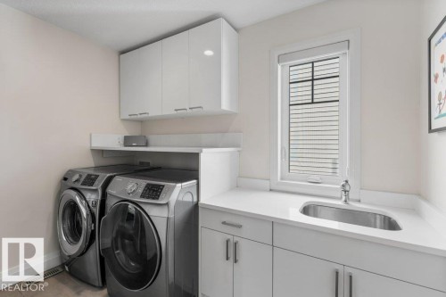 Upstairs Laundry area featuring white cabinetry, a countertop with an integrated sink, and Front Load Washer/Dryer - 4476 Suzanna Crescent, Edmonton, AB - Indoor Photo Showing Laundry Room