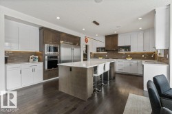 Kitchen Features Dark Hardwood Flooring, Two Tone Kitchen Cabinets, Gas Stove, Wall Oven, and White Quartz Counters - 