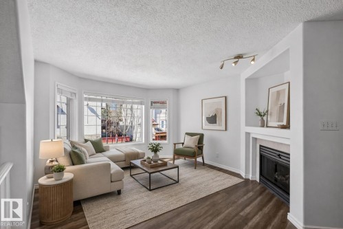 Living space featuring wood-finish flooring, a bay window with multiple panes, a built-in fireplace, recessed shelving, and track lighting - 6 1237 Carter Crest Road, Edmonton, AB - Indoor Photo Showing Living Room With Fireplace
