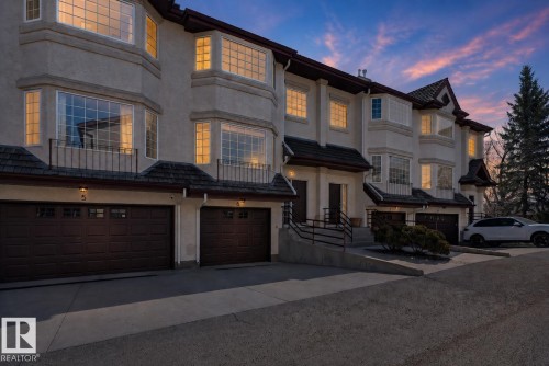 Stucco exterior featuring multiple bay windows, dark wood garage doors with window inserts, individual covered entryways, and wrought iron balcony railings - 6 1237 Carter Crest Road, Edmonton, AB - Outdoor With Facade