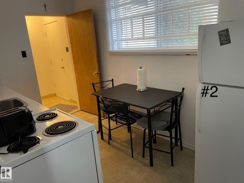 Compact kitchen area featuring a white electric range, stainless steel sink, and a white refrigerator - 10017 113 Street, Edmonton, AB 
