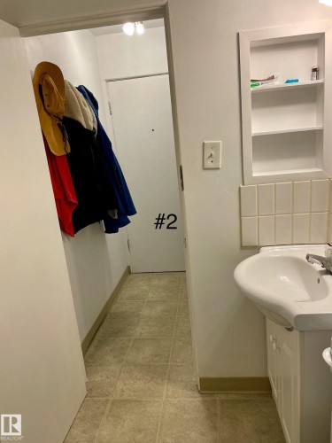 Pedestal-style sink with a dedicated vanity cabinet, built-in wall shelving, light-toned floor tile, and a wall-mounted light fixture - 10017 113 Street, Edmonton, AB 