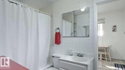Bathroom featuring a single vanity with a white countertop, a medicine cabinet with integrated lighting, white tiled walls, a white toilet, and a shower with a white curtain - 