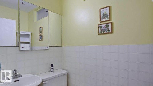 Bathroom featuring a white ceramic sink with chrome fixtures, a white toilet, white square wall tiling, a built-in medicine cabinet, and a wall-mounted storage unit - 10017 113 Street, Edmonton, AB 