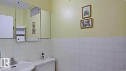 Bathroom featuring a white ceramic sink with chrome fixtures, a white toilet, white square wall tiling, a built-in medicine cabinet, and a wall-mounted storage unit - 