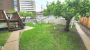 Expansive grassy yard featuring a mature tree, concrete pathway, and a wooden deck with railing - 10017 113 Street, Edmonton, AB 