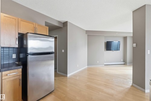 Kitchenette featuring stainless steel appliance, wood cabinetry, and a dark tile backsplash - 901 10504 99 Avenue, Edmonton, AB 
