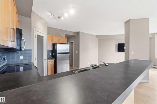 Kitchen featuring dark countertops, light wood cabinetry, stainless steel appliances, a tile backsplash, and a double basin sink with a gooseneck faucet - 901 10504 99 Avenue, Edmonton, AB 