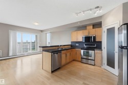 Open-concept kitchen featuring light wood cabinetry, stainless steel appliances, dark countertops, and a dark tile backsplash - 