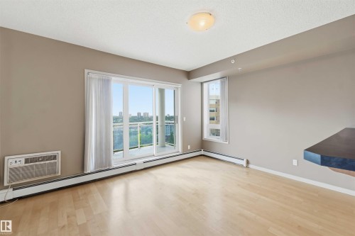 Open-concept interior featuring wood-finish flooring, a large balcony with glass railing, and a built-in air conditioning unit - 901 10504 99 Avenue, Edmonton, AB 