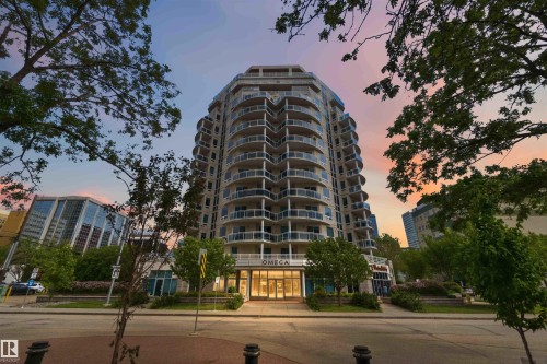 Modern high-rise building featuring a curved architectural design, individual balconies with glass railings, a prominent ground-level entrance, and surrounding mature trees - 901 10504 99 Avenue, Edmonton, AB 