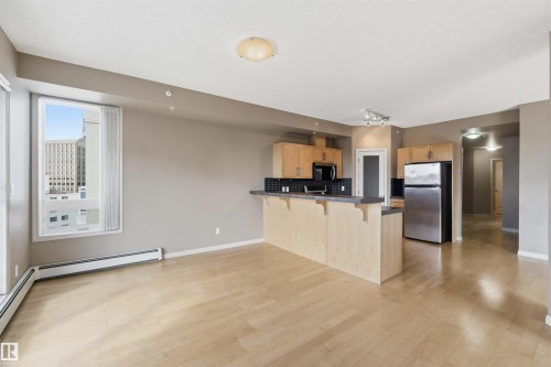 Open-concept living space featuring wood-finish flooring, a contemporary kitchen, light wood cabinetry, a breakfast bar with dark countertop, and large windows - 901 10504 99 Avenue, Edmonton, AB 