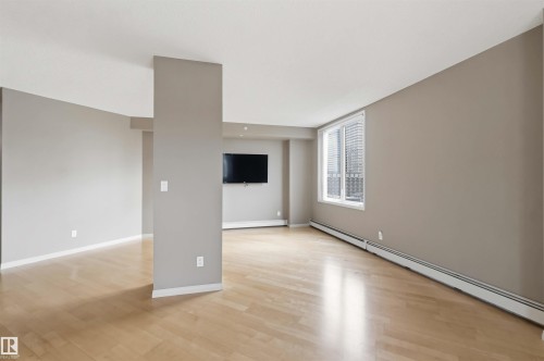 Spacious interior room featuring light wood-finish flooring, neutral paint tones, and a large window with horizontal blinds - 901 10504 99 Avenue, Edmonton, AB 