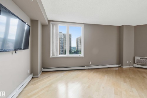 Spacious room featuring wood-finish flooring, neutral-toned walls, and a large window with vertical blinds - 901 10504 99 Avenue, Edmonton, AB 