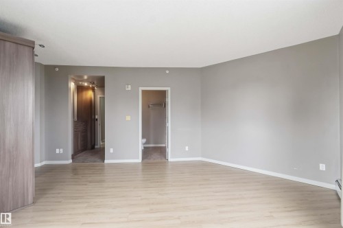 Spacious room featuring light wood-finish flooring, neutral gray walls, and white baseboards - 901 10504 99 Avenue, Edmonton, AB 