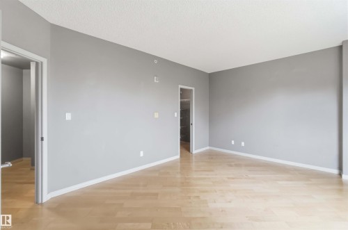 Spacious room featuring light wood-finish flooring, neutral gray wall paint, white trim, and two doorways - 901 10504 99 Avenue, Edmonton, AB 