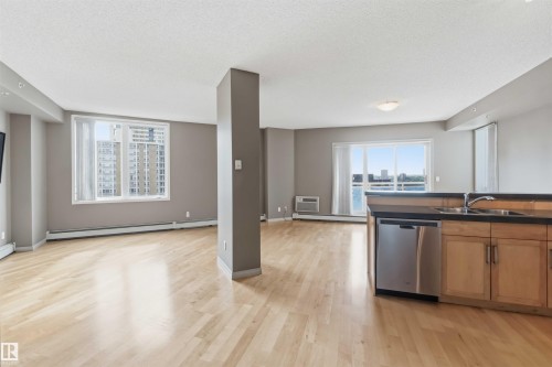 Open-concept living area with light wood-finish flooring, neutral gray walls, and large windows - 901 10504 99 Avenue, Edmonton, AB 
