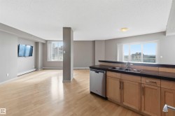 Open-concept living area featuring light wood-finish flooring, a kitchen peninsula with a double basin sink, stainless steel dishwasher, and natural wood cabinetry - 