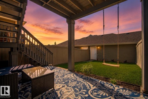 Covered patio area featuring a private grass yard, wood privacy fencing, and an exterior staircase - 4013 Blackbird Link, Edmonton, AB 