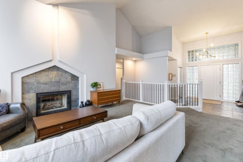Living area featuring a stone-faced fireplace with a hearth, vaulted ceilings, and a decorative railing overlooking the entry - 10 Everest Crescent, St. Albert, AB 