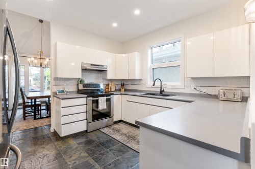 Modern kitchen featuring dark slate-style flooring, white flat-panel cabinetry, light gray countertops, and stainless steel appliances - 10 Everest Crescent, St. Albert, AB 