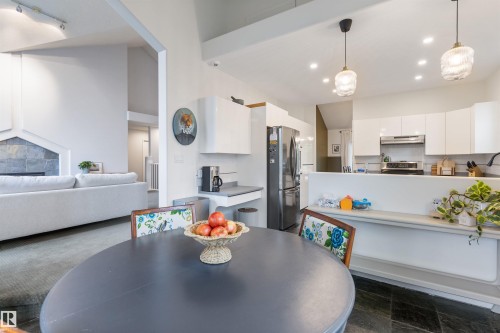 Open concept living area featuring dark slate flooring, a kitchen with white cabinetry and stainless steel appliances, and a stone fireplace with a white mantel - 10 Everest Crescent, St. Albert, AB 