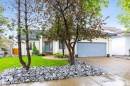Exterior featuring a light-colored stucco finish, gray shingled roof, an attached two-car garage with a light blue door, a concrete driveway, and a front yard with manicured lawn and decorative rock landscaping - 10 Everest Crescent, St. Albert, AB 