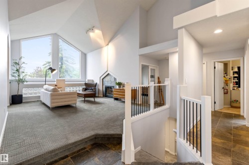 Vaulted ceiling living area featuring large windows, a built-in fireplace with stone surround, glass block accents, and an elevated carpeted floor - 10 Everest Crescent, St. Albert, AB 