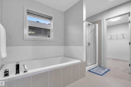 Bathroom featuring a built-in tub with white subway tile surround, a separate glass-enclosed shower, and light-toned floor tiling - 1616 157 Street, Edmonton, AB 