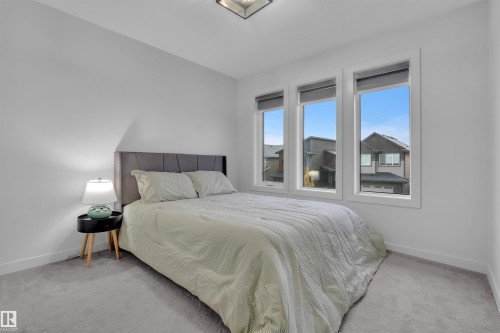Bedroom featuring three large vertical windows, light gray carpet, white walls, and a ceiling-mounted light fixture - 1616 157 Street, Edmonton, AB 