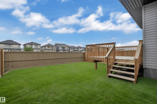 Expansive backyard featuring a natural wood deck with stairs and railing, a privacy fence, and a manicured lawn - 1616 157 Street, Edmonton, AB 