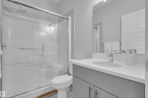 Bathroom featuring a shower with sliding glass doors, a vanity with a white countertop, an undermount sink, and a large mirror - 1616 157 Street, Edmonton, AB 