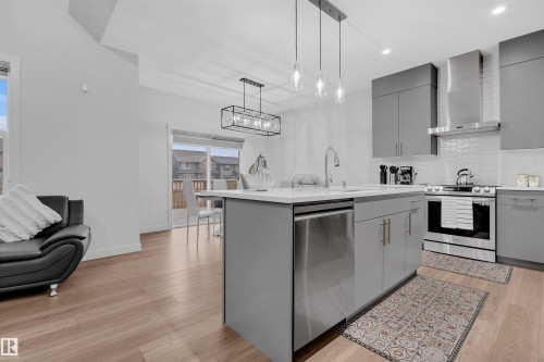 Modern kitchen featuring gray cabinetry, stainless steel appliances, a center island with sink, pendant lighting, and a white subway tile backsplash - 1616 157 Street, Edmonton, AB 