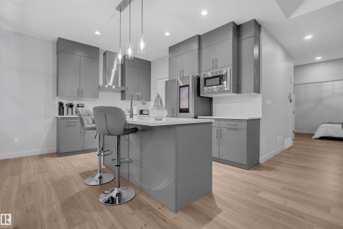 Modern kitchen featuring gray cabinetry, stainless steel appliances, a center island with seating, pendant lighting, and wood-finish flooring - 1616 157 Street, Edmonton, AB 