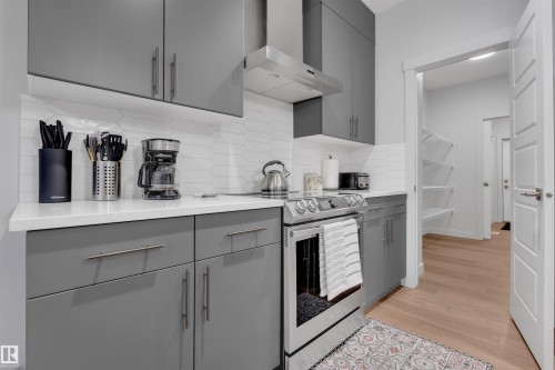 Modern kitchen featuring gray flat-panel cabinetry with brushed nickel hardware, white stone-finish countertops, and a white geometric tile backsplash - 1616 157 Street, Edmonton, AB 