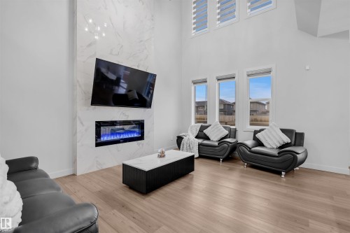 Living area featuring a tall ceiling, wood-finish flooring, a full-height marble-look fireplace surround with an integrated electric fireplace, and three upper transom windows with horizontal blinds - 1616 157 Street, Edmonton, AB 