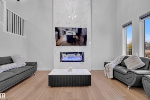 Vaulted ceiling living area featuring a floor-to-ceiling marble-look fireplace surround, built-in electric fireplace, light wood-finish flooring, and a modern stair railing - 1616 157 Street, Edmonton, AB 
