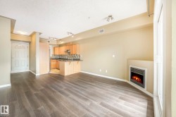 Open-concept living space featuring wood-finish flooring, a built-in fireplace, a kitchen with light wood cabinetry and dark countertops, and track lighting - 