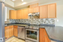 Kitchen featuring wood cabinetry, stainless steel appliances, mosaic tile backsplash, dark countertops, and recessed lighting - 