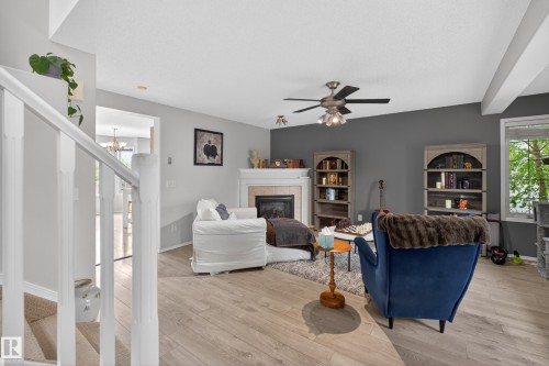Living area featuring a fireplace with a white mantel, light wood-finish flooring, a ceiling fan with integrated lighting, and a white framed window - 8 Vega Avenue, Spruce Grove, AB - Indoor With Fireplace