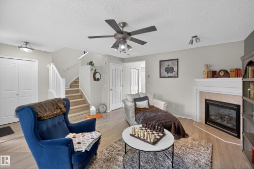 Living area featuring light wood-finish flooring and a corner fireplace with a white mantel and light tile surround - 8 Vega Avenue, Spruce Grove, AB - Indoor Photo Showing Living Room With Fireplace