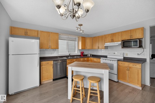 Kitchen featuring light wood cabinetry, dark countertops, and wood-finish flooring - 8 Vega Avenue, Spruce Grove, AB - Indoor Photo Showing Kitchen With Double Sink