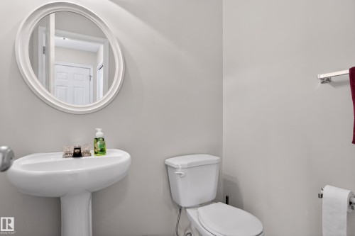 Pedestal sink with oval mirror, chrome fixtures, and white toilet - 8 Vega Avenue, Spruce Grove, AB - Indoor Photo Showing Bathroom