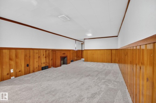 Spacious room featuring light gray carpeting, wood paneling, a built-in fireplace with brick detailing, white walls, and a white ceiling with recessed lighting - 9740 65 Avenue Nw, Edmonton, AB 